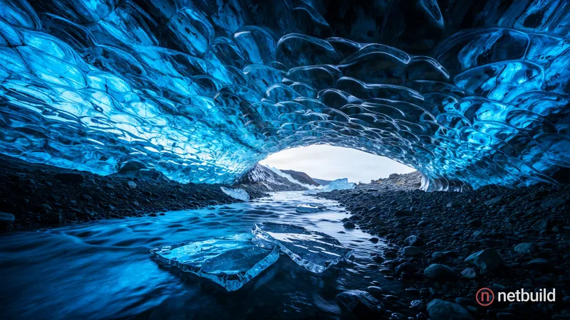 A wide-angle landscape photograph inside a sprawling, low-ceilinged ice cave awash in vibrant sapphire and cyan hues. The deeply textured, rippled tra...